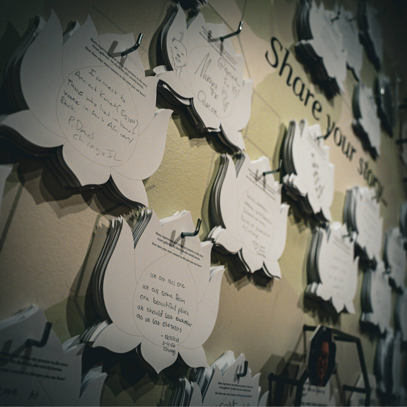 A close-up of a wall full of lotus-shaped cards with stories written on them. The text "Share your story" is visible on the wall.